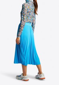 Blå plisserad kjol med texturerad tyg, kombinerad med en långärmad blommig topp. Bärs med gråa och vita träningsskor.