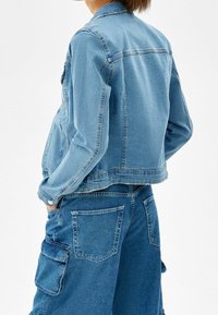 Ljust blå denimjacka med en kortad design, knappstängning, två framfickor och en något fransad nederkant. Matchas med matchande denimbyxor.