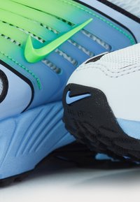 Sneakers med ett vitt och blått övermaterial, gröna och blå accenter, texturerat nätmaterial och en framträdande svart gummisula med en liten logotyp.