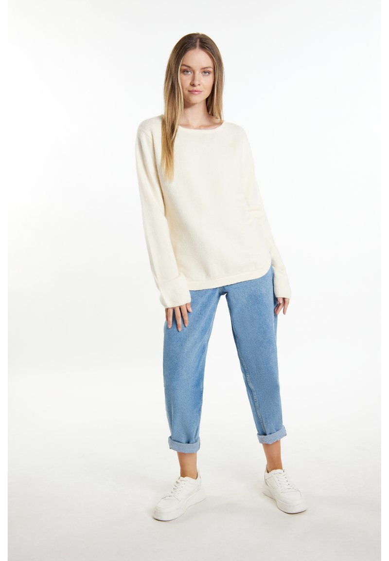 Cremfarbener Oversized-Pullover mit Rundhalsausschnitt und langen Ärmeln, kombiniert mit hellblauen Jeans mit hochgekrempelten Säumen und weißen Sneakers.