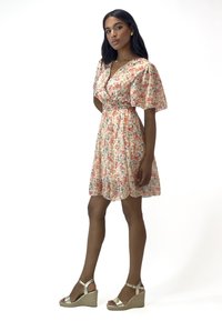 Robe florale avec de courtes manches bouffantes, taille cintrée et jupe en A. Les couleurs incluent pêche, rose, vert et bleu. Sandales compensées en argent.