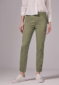 Zelené cargo kalhoty se slim fit střih, dvě boční kapsy a hladkou texturu. V kombinaci s bílými teniskami a bílou košilí na knoflíky.