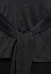 Gros plan d'un tissu noir texturé noué en un nœud simple, montrant les détails et le tissage du matériau.