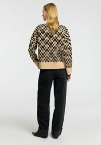 Neulepusero beigen ja mustan sävyissä, jossa on geometrisia kuvioita. Yhdistetty korkeavyötäröisten tummansinisien farkkujen ja mustien nilkkasaappaiden kanssa.