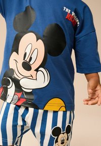 Blå T-shirt med et stort Mickey Mouse print, kortærmet, parret med hvide og blå stribede shorts med et lille Mickey emblem.