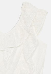 Robe en dentelle blanche avec détails volants aux épaules. Tissu texturé avec un éclat subtil, design léger et qui tombe doucement.