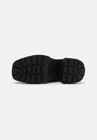 Suela de bota de goma negra con surcos profundos y patrones elevados. Textura suave y diseño estructurado, adecuado para agarre y durabilidad.