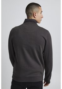 Felpa in pile grigio scuro con colletto alto, polsini e orlo a costine. Presenta dettagli di cucitura e una superficie liscia sul retro.