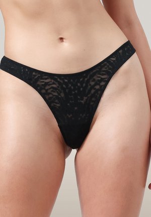 Zwarte semi-doorzichtige kant bikini-stijl ondergoed op de heupen en bovenbenen van een persoon tegen een neutrale achtergrond.