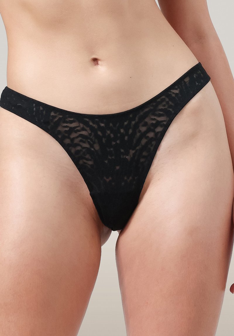 Zwarte semi-doorzichtige kant bikini-stijl ondergoed op de heupen en bovenbenen van een persoon tegen een neutrale achtergrond.