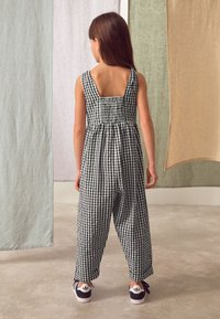 Tuta a quadretti bianco e nero con corpetto arricciato, gambe larghe e schiena quadrata. Abbinata a sneakers nere con dettagli bianchi.