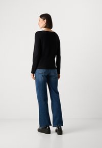 Schwarzes Langarmoberteil mit weitem Ausschnitt, kombiniert mit blauen weit geschnittenen Jeans und schwarzen Plateauschuhen. Einfaches, minimalistisches Design.