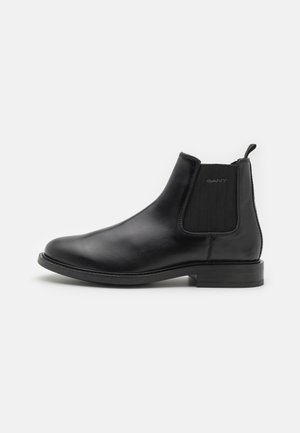 Black leather Chelsea boot with elastic side panels, rounded toe, and low block heel. Features stitching detail and a pull tab for easy wear.