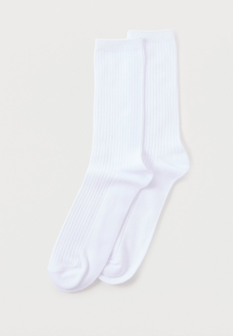 Ζευγάρι απλές λευκές ριμπ πλεκτές κάλτσες κανονικού μήκους απλωμένες σε φωτεινό φόντο.