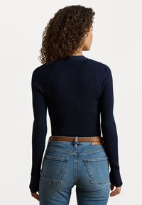 Navy ribbed long-sleeve top with a fitted design. Features raglan sleeves and a crew neckline, paired with light blue high-waisted jeans and a brown belt.