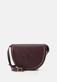 Borsa a tracolla in pelle borgogna con una forma curva, logo 'CK' impressa, hardware dorato e una tracolla staccabile e regolabile.