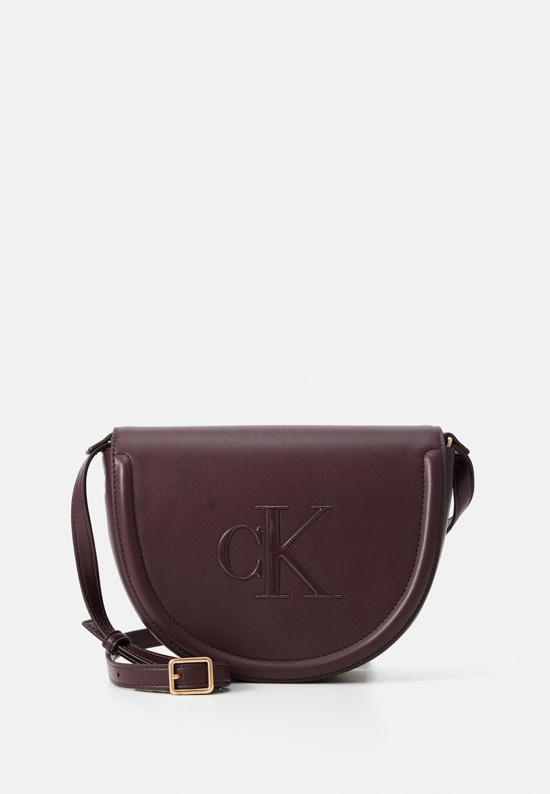 Borsa a tracolla in pelle borgogna con una forma curva, logo 'CK' impressa, hardware dorato e una tracolla staccabile e regolabile.