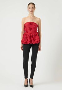 Rød off-shoulder top med 3D rosenudsmykninger, flared kant, parret med sorte leggings og sorte spidse hæle. Glat stof, livlig farve.