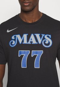 Czarny bawełniany t-shirt z napisem "MAVS" w niebieskim, ozdobnym stylu oraz numerem "77" w perforowanym niebieskim wzorze. Zawiera szare logo Nike.