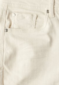 Tessuto di denim bianco con una tasca frontale, con cuciture visibili e rivetti metallici lucidi per i dettagli.