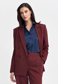 Burgundowa marynarka dwurzędowa w zestawieniu z granatową koszulą z guzikami. Strukturalny design, gładka tekstura i dopasowany krój.