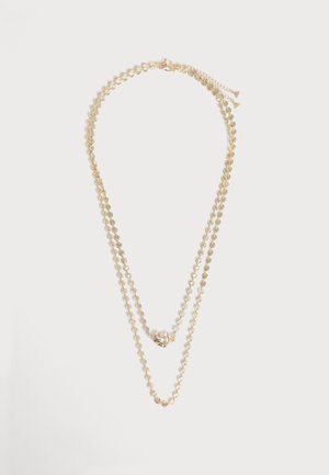 Doppellagige Goldkette mit kleinen blumenförmigen Gliedern und einem strukturierten Herz-Anhänger an der kürzeren Kette.