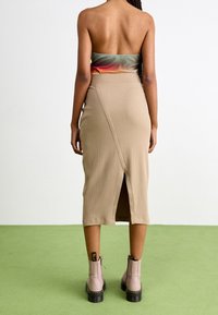 Falda midi de canalé beige con una abertura lateral, combinada con un top corto multicolor. La modelo lleva botas de tobillo rosa claro con detalles en negro.