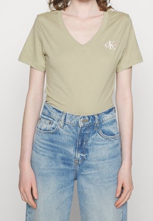 Jasnozielona bawełniana koszulka z dekoltem w serek, krótkimi rękawami i małym logiem po lewej stronie, zestawiona z niebieskimi dżinsami z wysokim stanem.