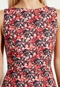 Šaty s květinovým potiskem a kulatým výstřihem v červených, bílých a tmavě fialových barvách, vyrobené z hladké látky s přiléhavým střihem.