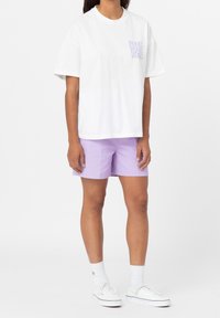 Bílý tričko s fialovým logem "Dickies", doplněné levandulovými šortkami. Oblečení má volný střih a je vyrobeno z bavlny.