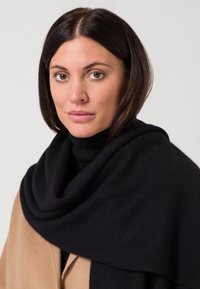 Châle en laine noire drapé sur un manteau beige, avec une texture douce et un design large et fluide autour des épaules et du décolleté.