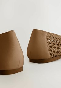 Bailarinas de cuero marrón con un diseño trenzado en el lateral, punta afilada y suela de goma plana. Textura suave con un acabado mate.