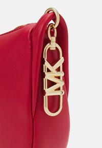 Sac en cuir rouge avec un fermoir en métal doré et un logo bien en vue. La texture est lisse avec une forme structurée.