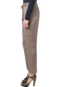 Kobieta nosząca taupe'owe spódnice tapered z elastycznym paskiem, granatową bluzkę z długim rękawem oraz metaliczne sandały na wysokim obcasie z frędzlami.