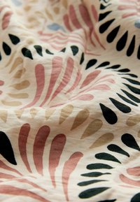 Tissu à fond crème présentant des formes abstraites en goutte d'eau en noir, rose, beige et vert foncé, montrant des plis doux et une texture.