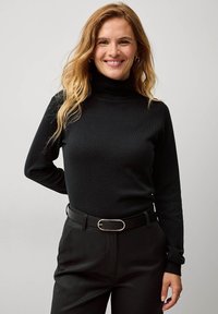 Maglione a collo alto di colore nero in tessuto a coste, design aderente, abbinato a pantaloni a vita alta e una cintura nera con fibbia metallica.