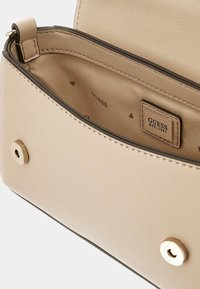 Sac à main en cuir beige avec une texture lisse, des accessoires en or et une discrète étiquette de logo à l'intérieur. Il est doté d'une fermeture à pression sécurisée.