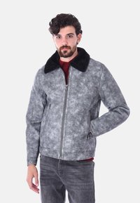 Giacca in finta pelle grigia con colletto in pelliccia nera, frontale con zip e due tasche laterali; presenta una finitura texturizzata e una vestibilità sartoriale.