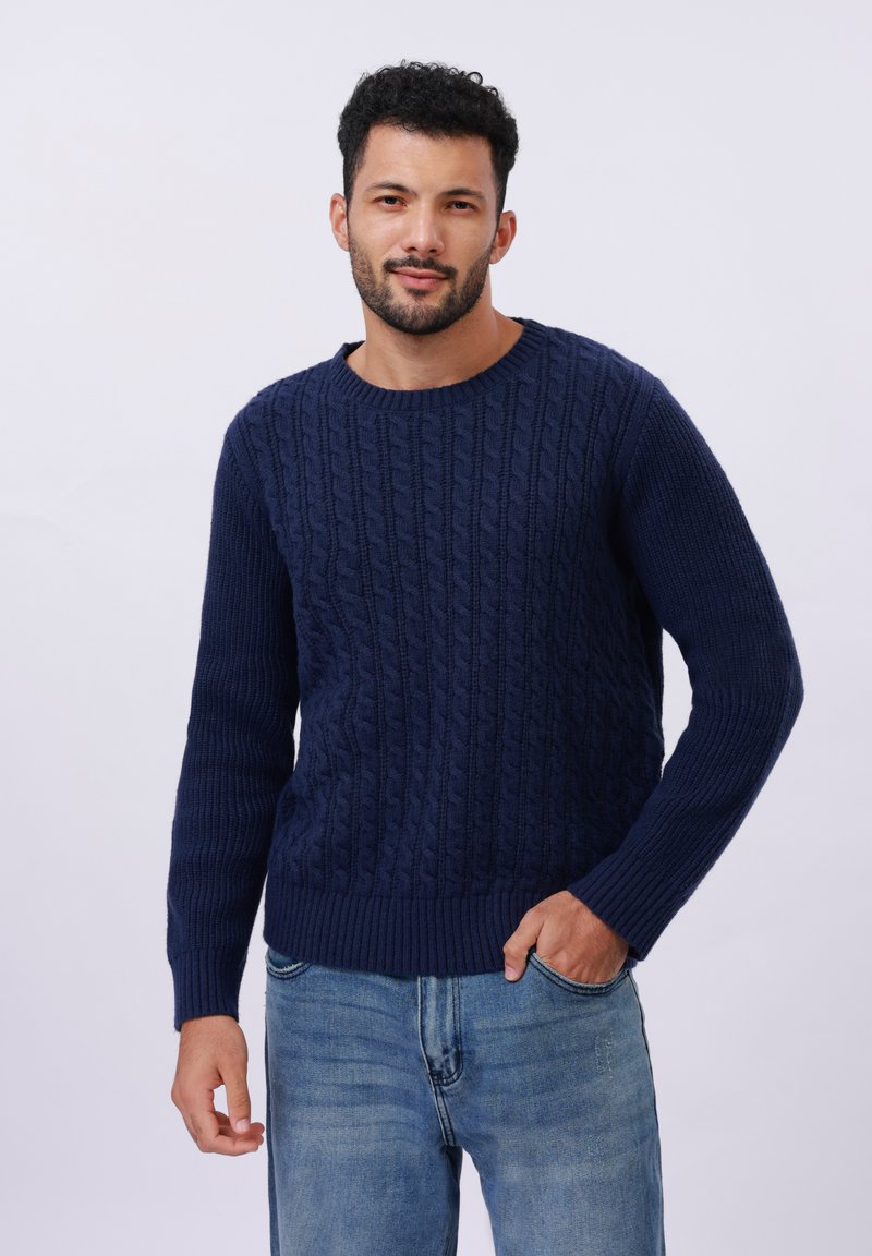 Navy blue cable-knit sweater made from textured knit fabric with a round neckline and ribbed cuffs and hem, worn with light blue jeans.