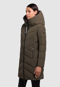 Olivroheline puffernakke, millel on chevron-õmblemise disain, kõrge kaelus ja esine lukku. Omab küljetaskuid ja logo aktsenti.