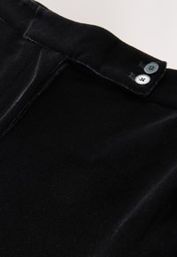 Mustast sametist kangas, millel on sile tekstuur, vöökohal kaks hõbedast nuppu ja korrapäraselt viimistletud äär.