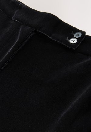 Črno žametno blago z gladko teksturo, z dvema srebrnima gumboma na pasu in lepo zaključeno robom.