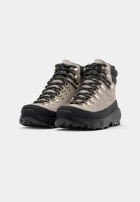 Botas de caminhada de cano médio em bege claro e preto. As características incluem ilhós metálicos, atacadores pretos, sola de borracha ranhurada e texturas contrastantes.