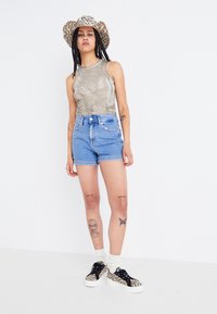 Olivenfarget ermeløs topp, høyt liv lys blå denimshorts, leopardmønstret hatt og svarte joggesko med hvit såle og mønstrete detaljer.