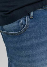 Vaqueros de mezclilla azul medio con un sutil desgaste, que cuentan con un bolsillo delantero con costuras naranjas y una apertura de bolsillo redondeada.