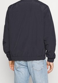 Granatowa, lekka kurtka z elastycznymi mankietami i paskiem w talii, o prostym wzorze i gładkiej teksturze, z detalem w postaci karczku z tyłu.