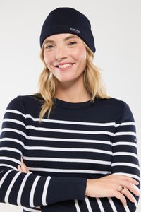 Beanie blu navy con texture a costine, abbinato a un maglione a righe blu navy e bianche con scollo rotondo e dettaglio con bottoni sulle spalle.