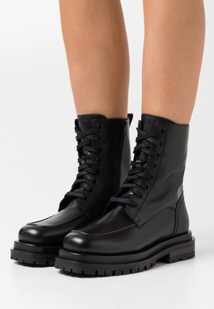 Bottines en cuir noir avec lacets et fermeture éclair latérale. Semelle en caoutchouc épaisse avec finition texturée. Tige lisse avec des détails de couture minimaux.
