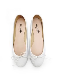 Ballerines blanches en cuir lisse avec un bout rond, une accentuation en nœud, et une semelle intérieur beige portant le nom de la marque imprimé.