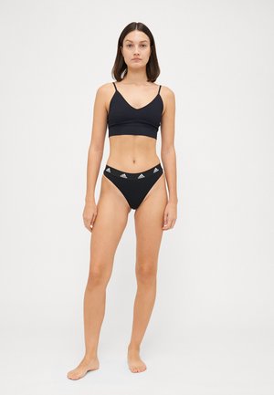 Musta urheiluliivi syvällä V-pääntiellä, yhdistettynä mustiin bikinityylisiin alaosiin, joissa on valkoinen Adidas-logo. Silkkinen pinta ja minimalistinen tyyli.
